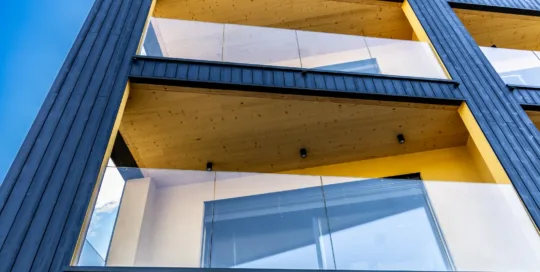 Edificio moderno con facciata in legno scuro e balconi a sbalzo con parapetti in vetro. Homeled Cylinder Neri