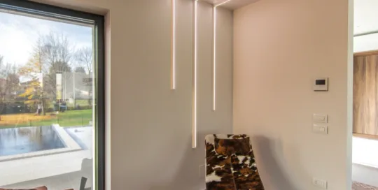 Interno di una casa moderna con arredi di design, illuminazione a LED e vista su un piscina e giardino.