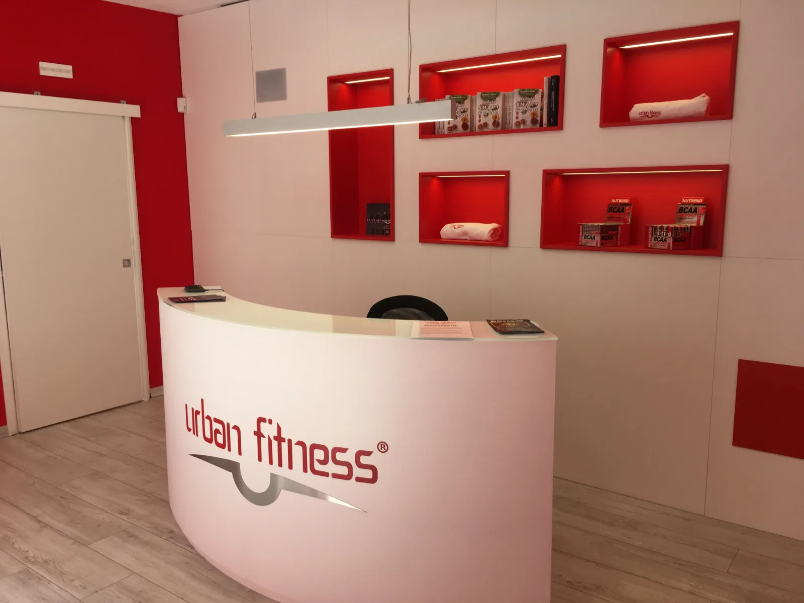 Reception moderna di una palestra Urban Fitness con design rosso e bianco.