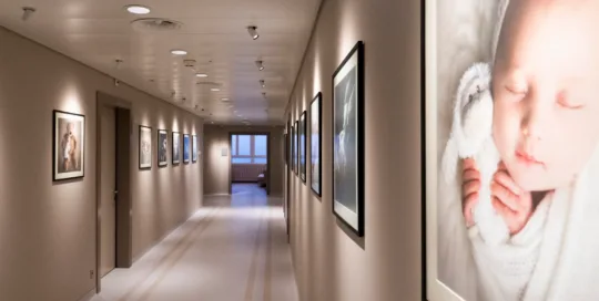 Corridoio di ospedale illuminato con fotografie di neonati incorniciate lungo le pareti. Illuminazione Spotty by Homeled