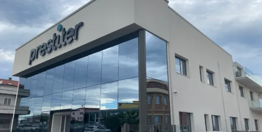 Edificio moderno con insegna Prestiter, vetrate riflettenti e auto parcheggiate davanti.