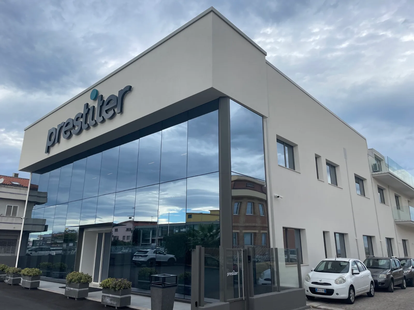 Edificio moderno con insegna Prestiter, vetrate riflettenti e auto parcheggiate davanti.